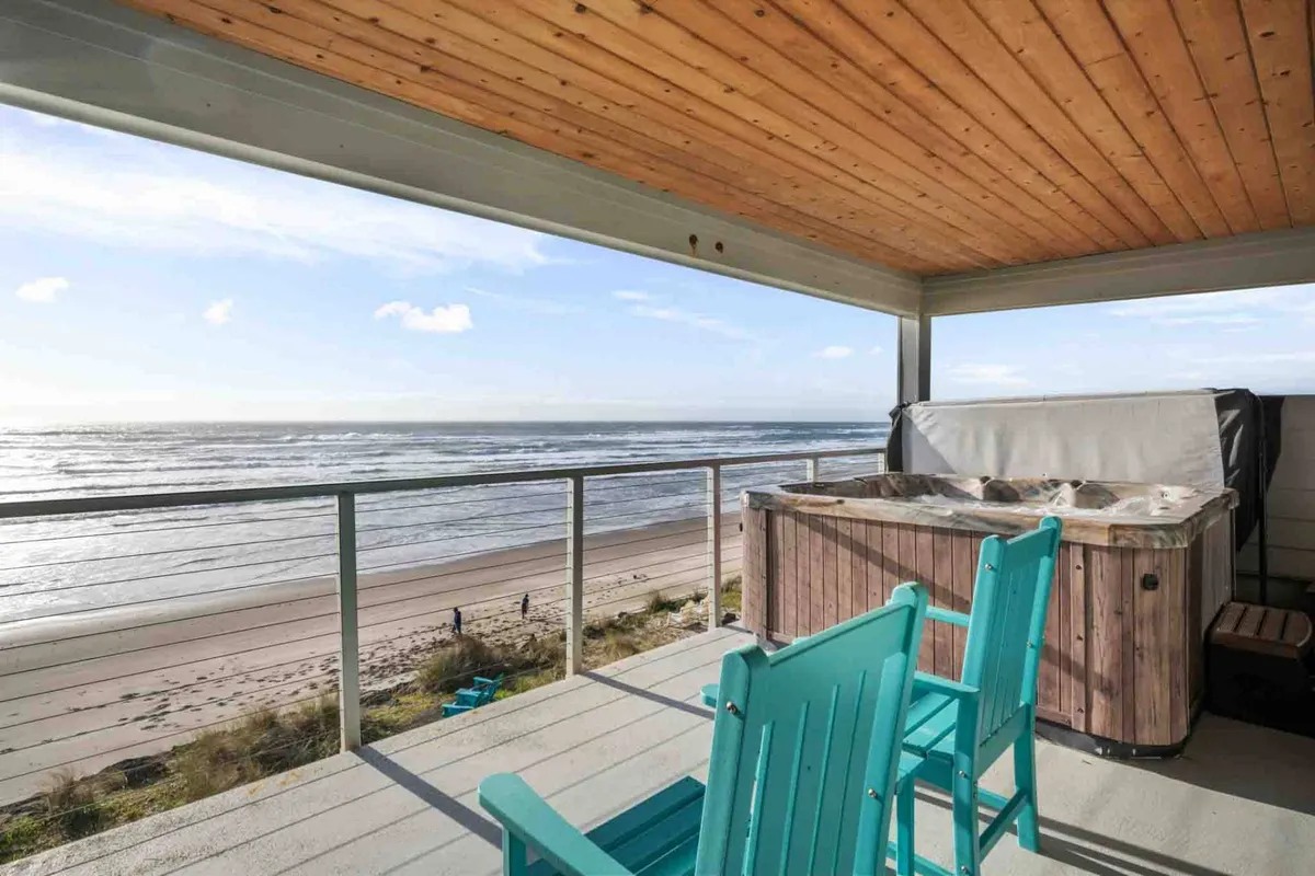 An inviting exterior scene featuring a hot tub overlooking the beach, with Adirondack chairs nearby and a sweeping view of the ocean. The setting sun creates a tranquil, golden ambiance that’s perfect for unwinding after a day by the sea.