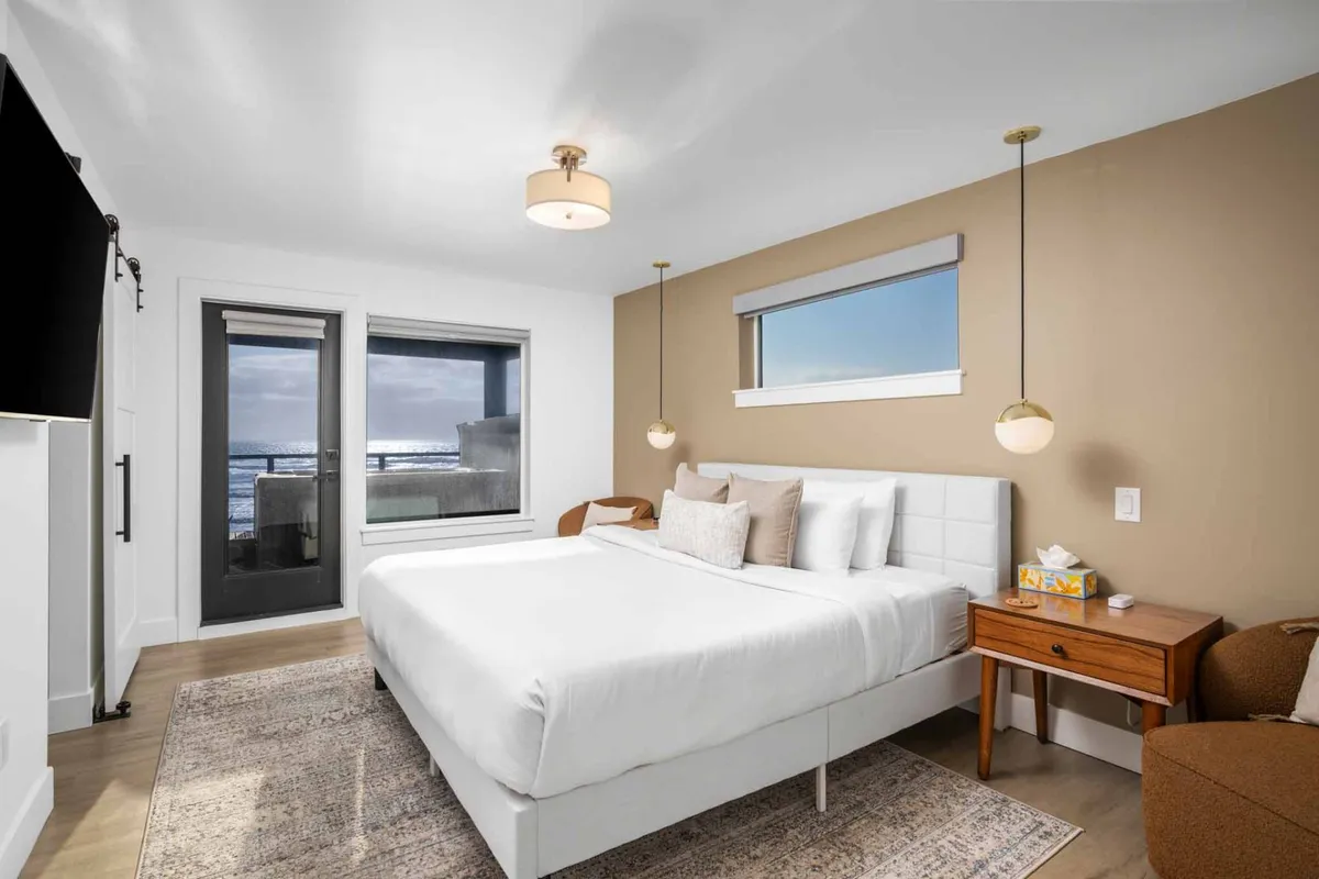 A serene bedroom featuring a plush bed positioned beside a large window showcasing a peaceful ocean view. The room is styled with a nightstand and lamp, creating an atmosphere ideal for relaxation, reading, and enjoying the calming scenery.