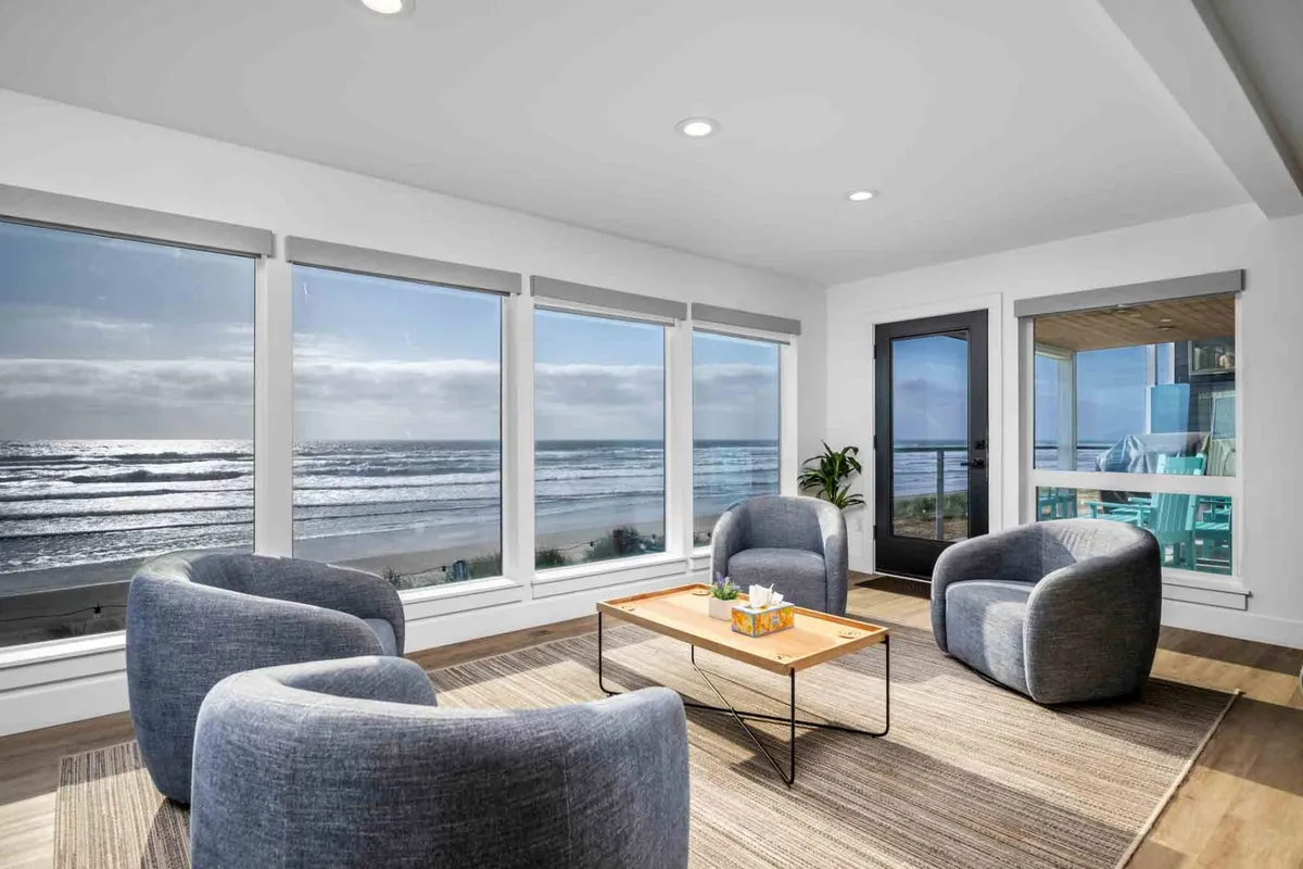 A bright living area with large windows offering a captivating ocean view. Comfortable seating is arranged around a coffee table with refreshments, inviting guests to relax while observing the waves and coastal scenery beyond the glass.