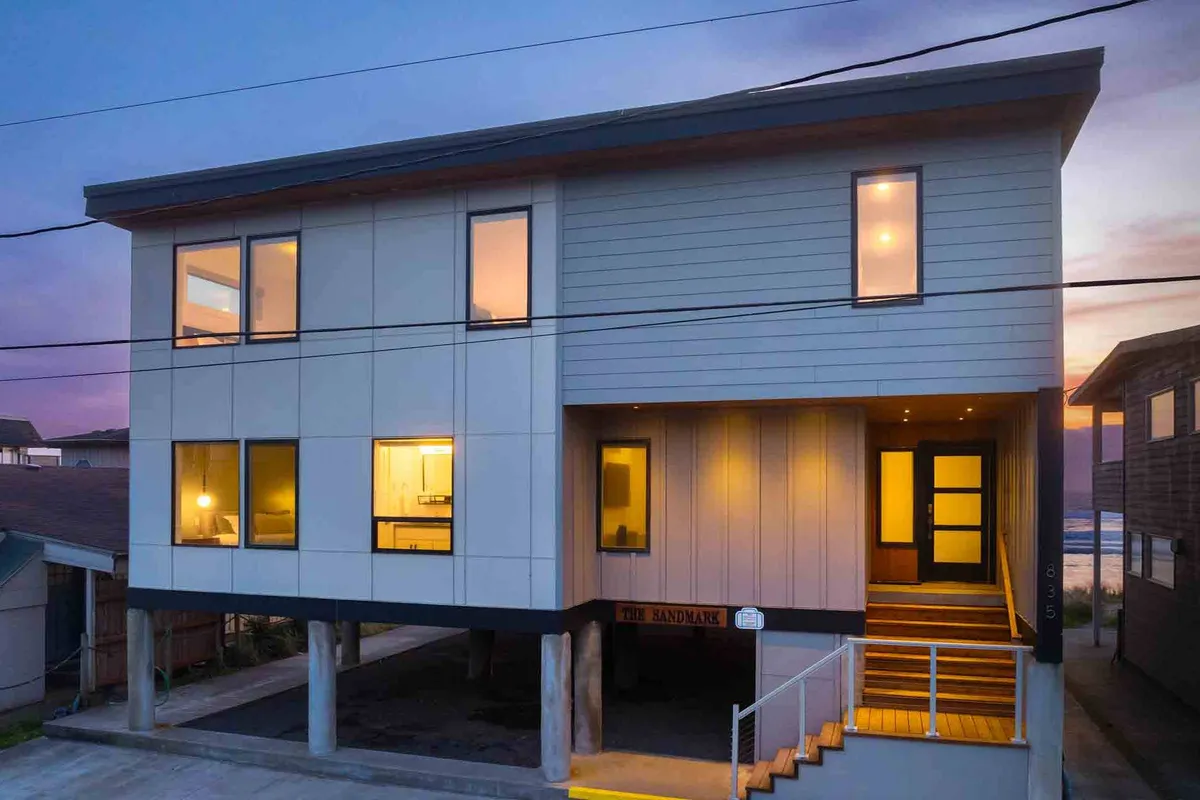 A modern exterior view of the property, this image shows illuminated windows and an inviting entrance, hinting at the luxurious interiors within. The design emphasizes privacy and contemporary elegance while still connecting to the surrounding landscape.