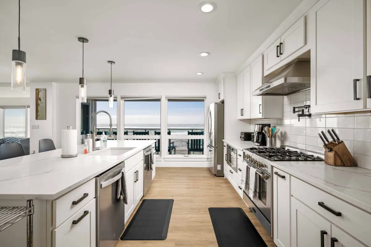 A modern kitchen features a large central island, state-of-the-art appliances, and floor-to-ceiling windows framing stunning ocean vistas. The design encourages cooking, entertaining, and socializing while soaking in the surrounding scenery.
