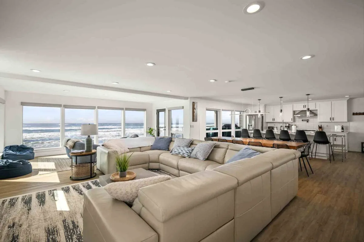 A stylish interior scene featuring a spacious sectional sofa facing large windows with unobstructed ocean views and a sleek kitchen island nearby. The setting radiates comfort and openness, perfect for gatherings, casual dining, or simply soaking in the scenery.